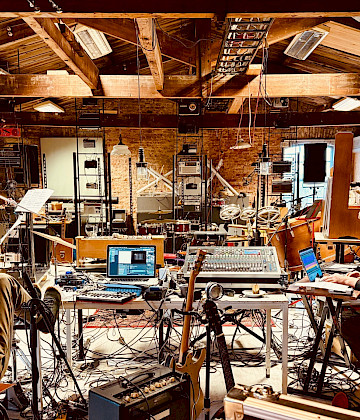 Muzikanten van Veenfabriek werken tussen instrumenten en geluidsapparatuur in de monumentale zolder van Scheltema in Leiden. Foto: Yonga Sun